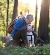 Kvinde sidder i en skov og kysser sin hund på hovedet.