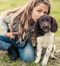 Pige og hvalp der sidder på jorden. Pige kysser hvalpen på hovedet.