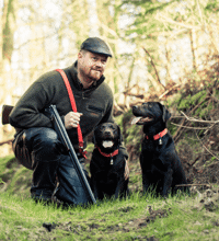 To sorte hunde der sidder ved siden af en jæger.