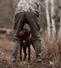 Hund der står mellem benene på en jæger, ude i en skov.
